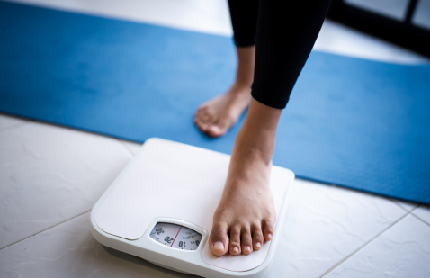 A woman using weighing machine as feature image for weight loss research blog